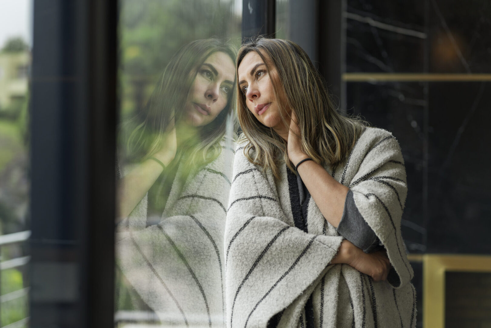 Woman wrapped in blanket gazing through window.